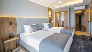 Quarto de hotel com duas camas, mesa de cabeceira, escrivaninha e luminária moderna.