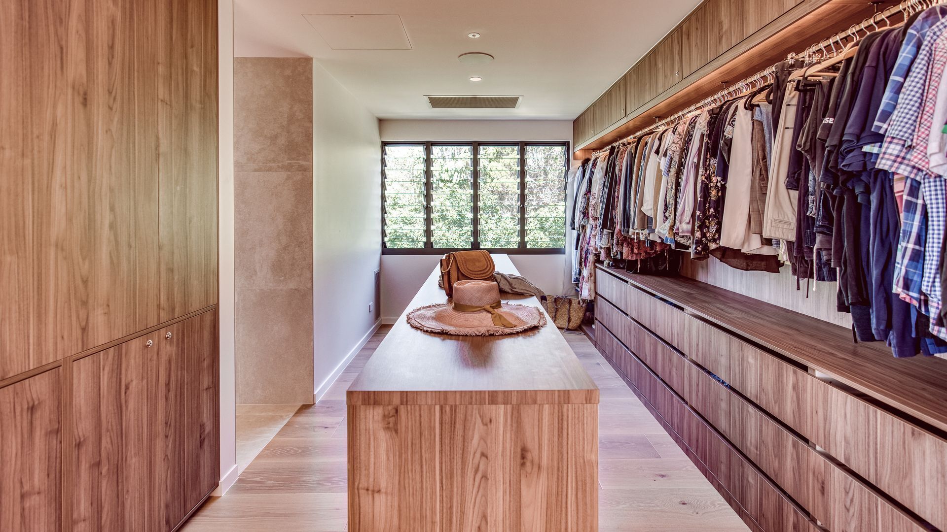 A walk-in closet with wooden cabinetry, a bench, and a clothing rack.