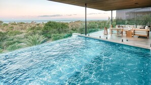 En modern infinitypool med utsikt över havet och frodig grönska.