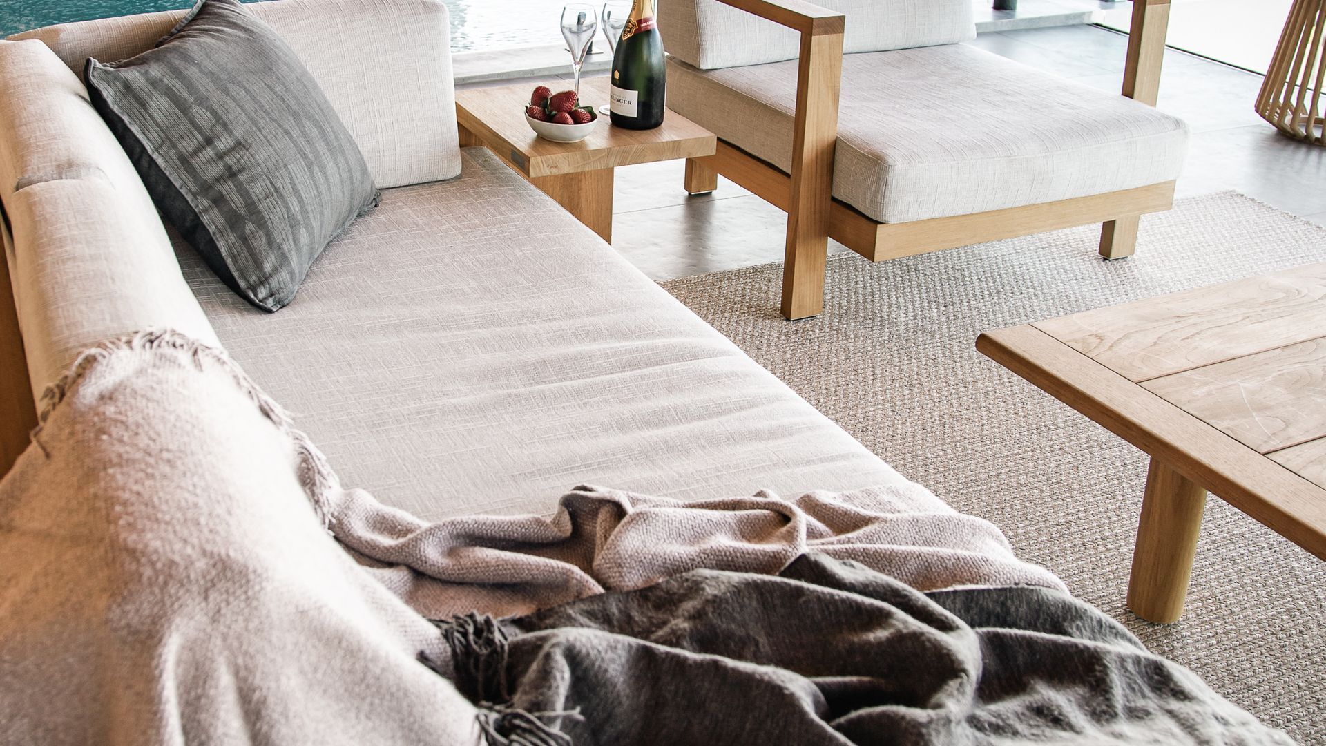 A modern living room with a sofa, a coffee table, and a chair. There is a bottle of champagne and a bowl of strawberries on the coffee table.