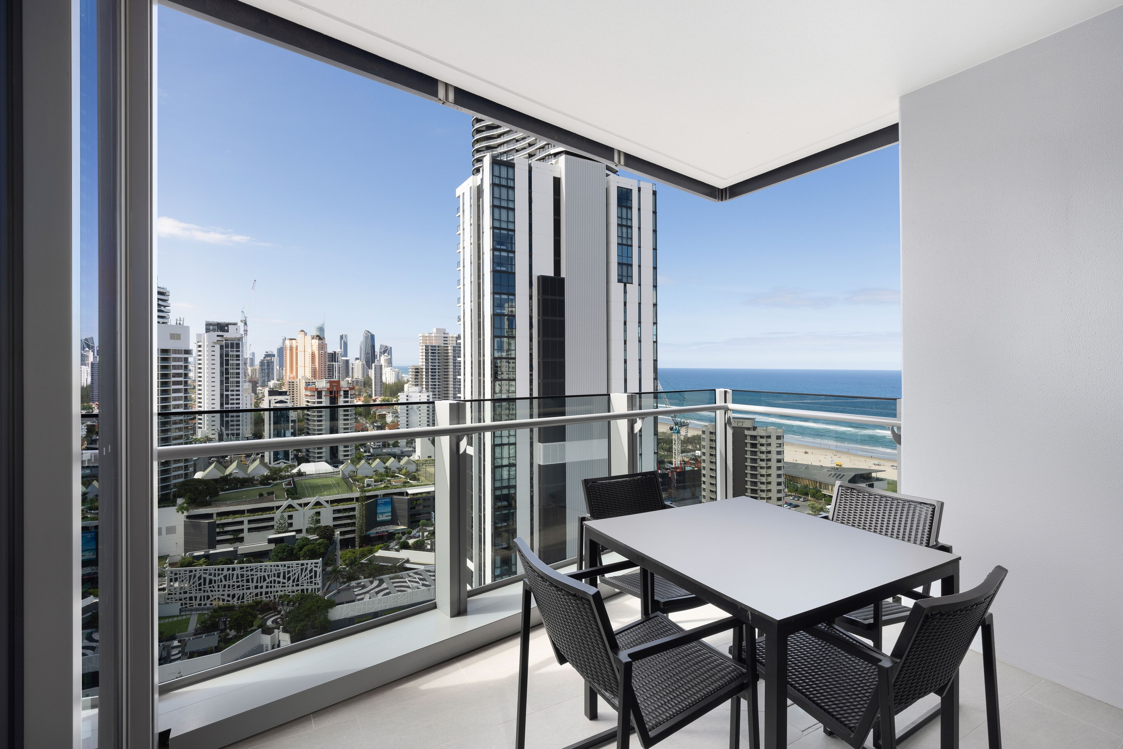 Un balcon avec une table et des chaises, offrant une vue sur le paysage urbain et la plage.