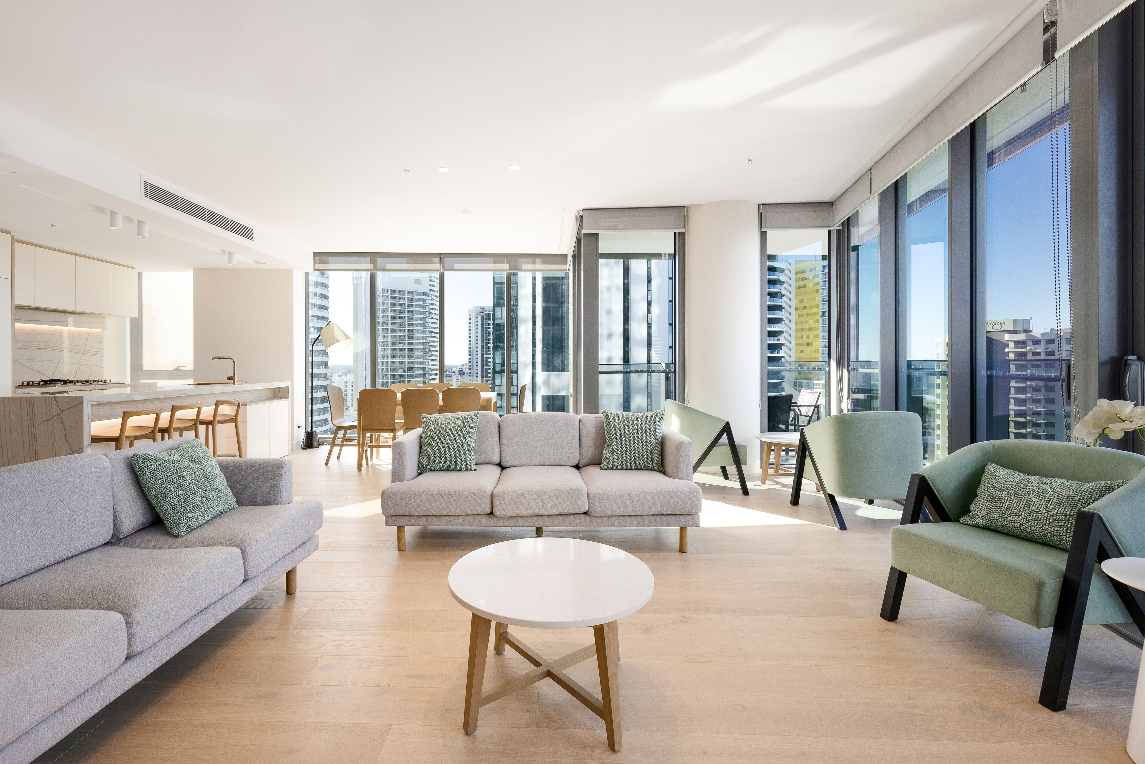 A modern living room with a sofa, armchairs, and a coffee table. There is a dining area with chairs and a table in the background.
