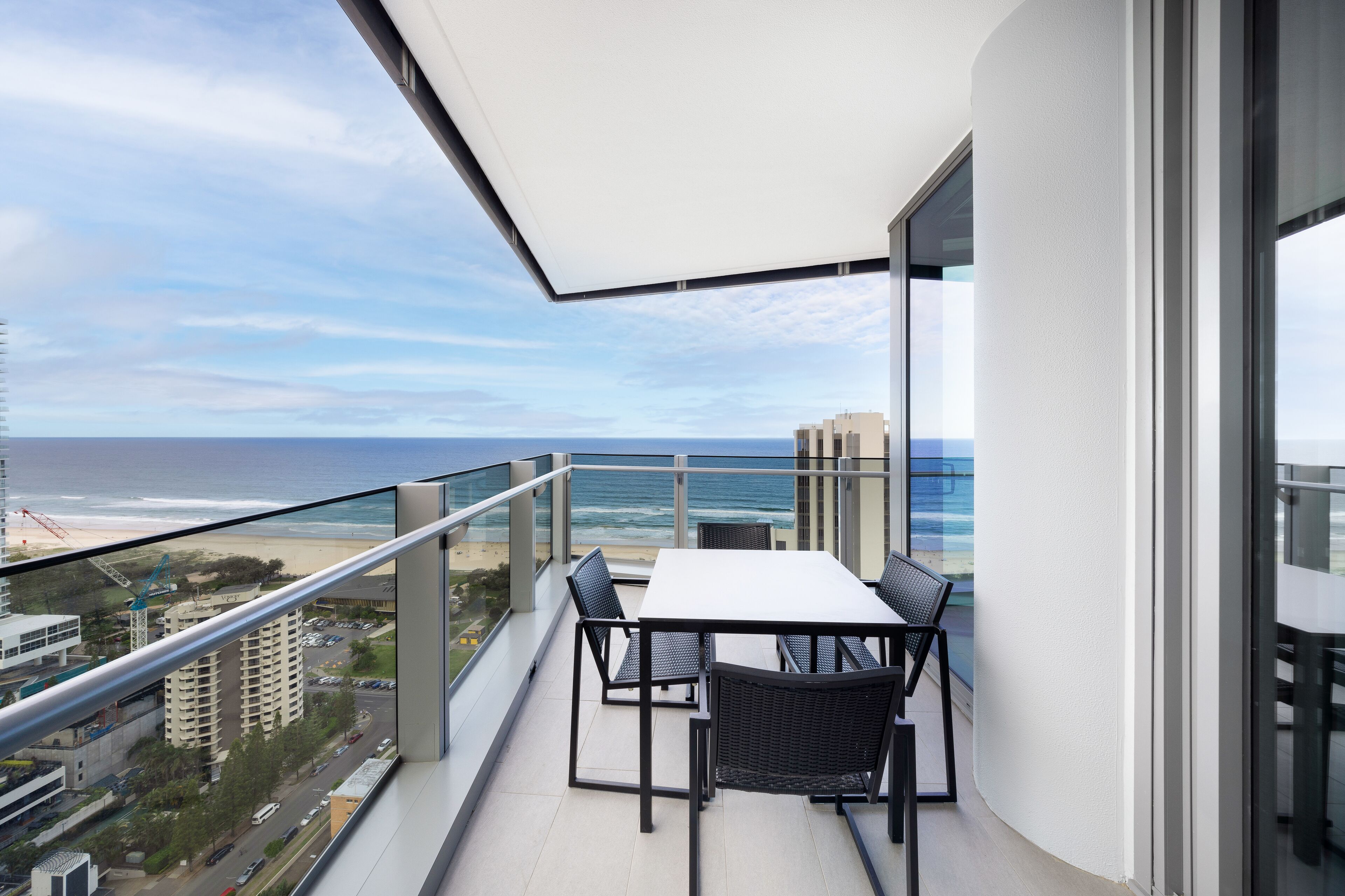 A balcony with a table and chairs, overlooking a beach and ocean.
