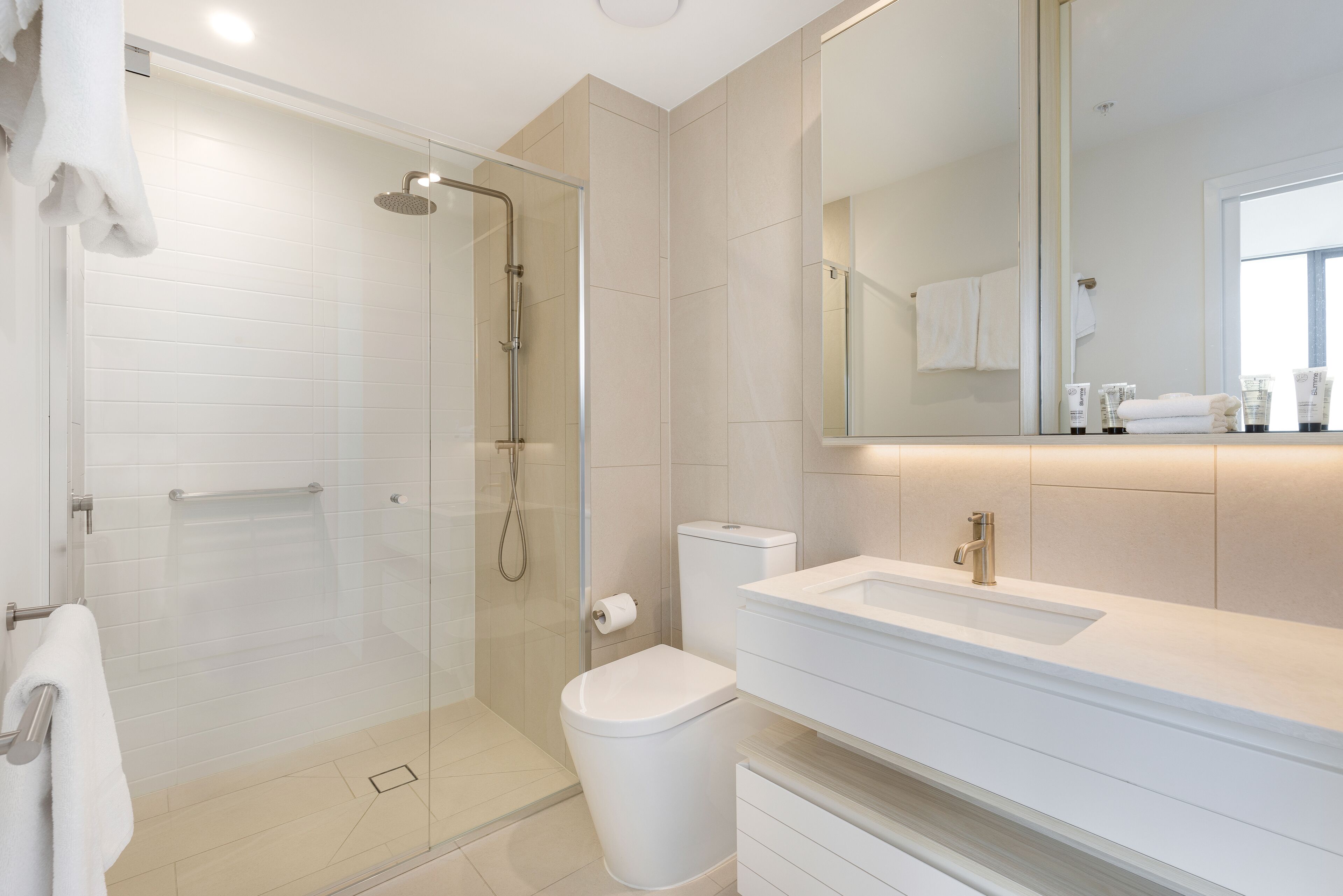 A modern bathroom with a glass-enclosed shower, a white toilet, and a vanity with a sink and mirror.