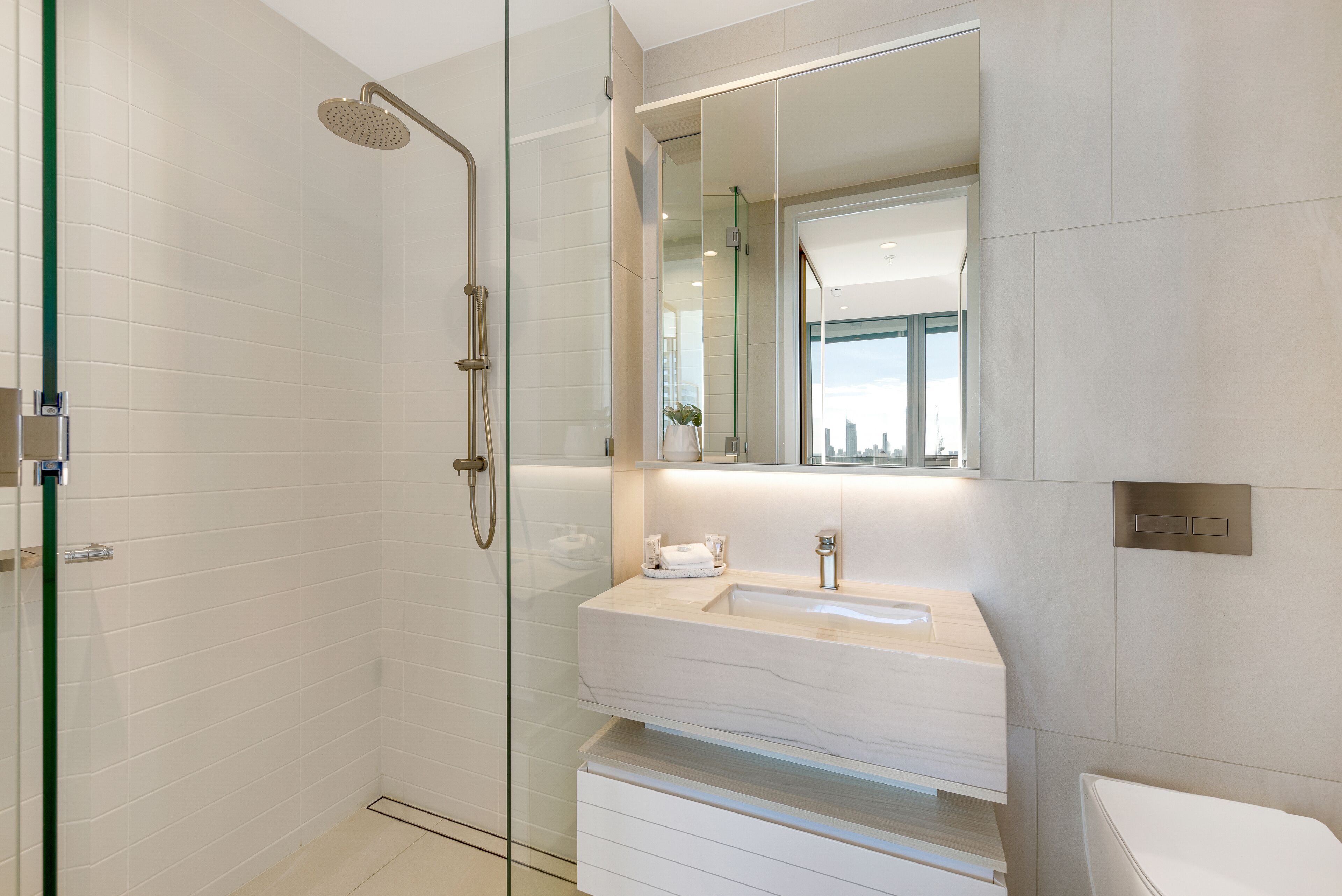 A modern bathroom with a glass-enclosed shower, a large mirror, and a white vanity with a sink.