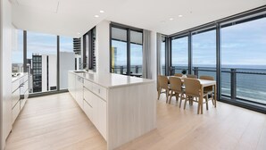 A modern kitchen with a central island, large windows, and a view of the ocean. - ULTIQA Signature at Broadbeach (Broadbeach)