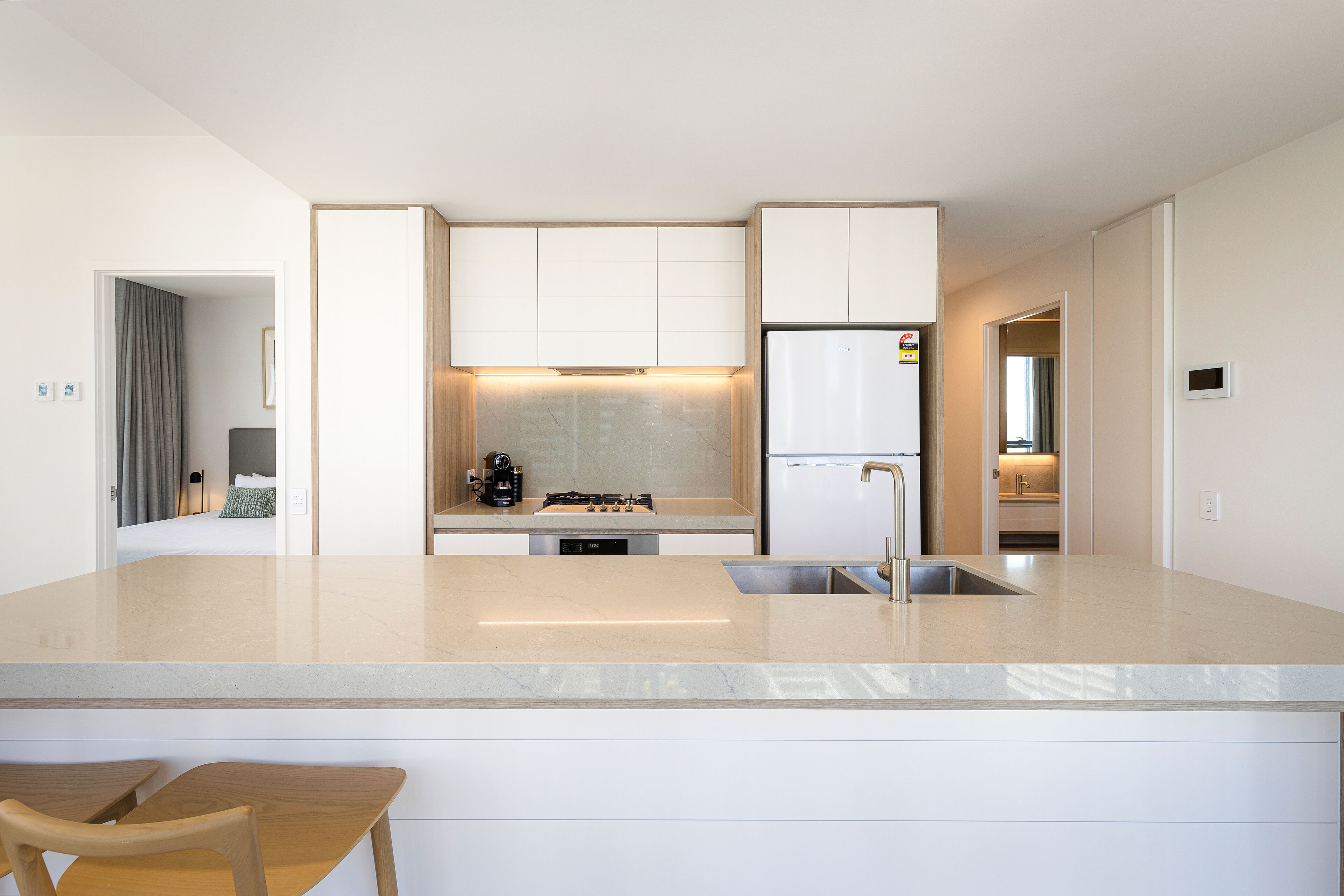 Una cocina moderna con una isla central, electrodomésticos integrados y vistas al dormitorio contiguo.