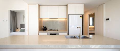 Una cocina moderna con una isla central, electrodomésticos integrados y vistas al dormitorio contiguo.