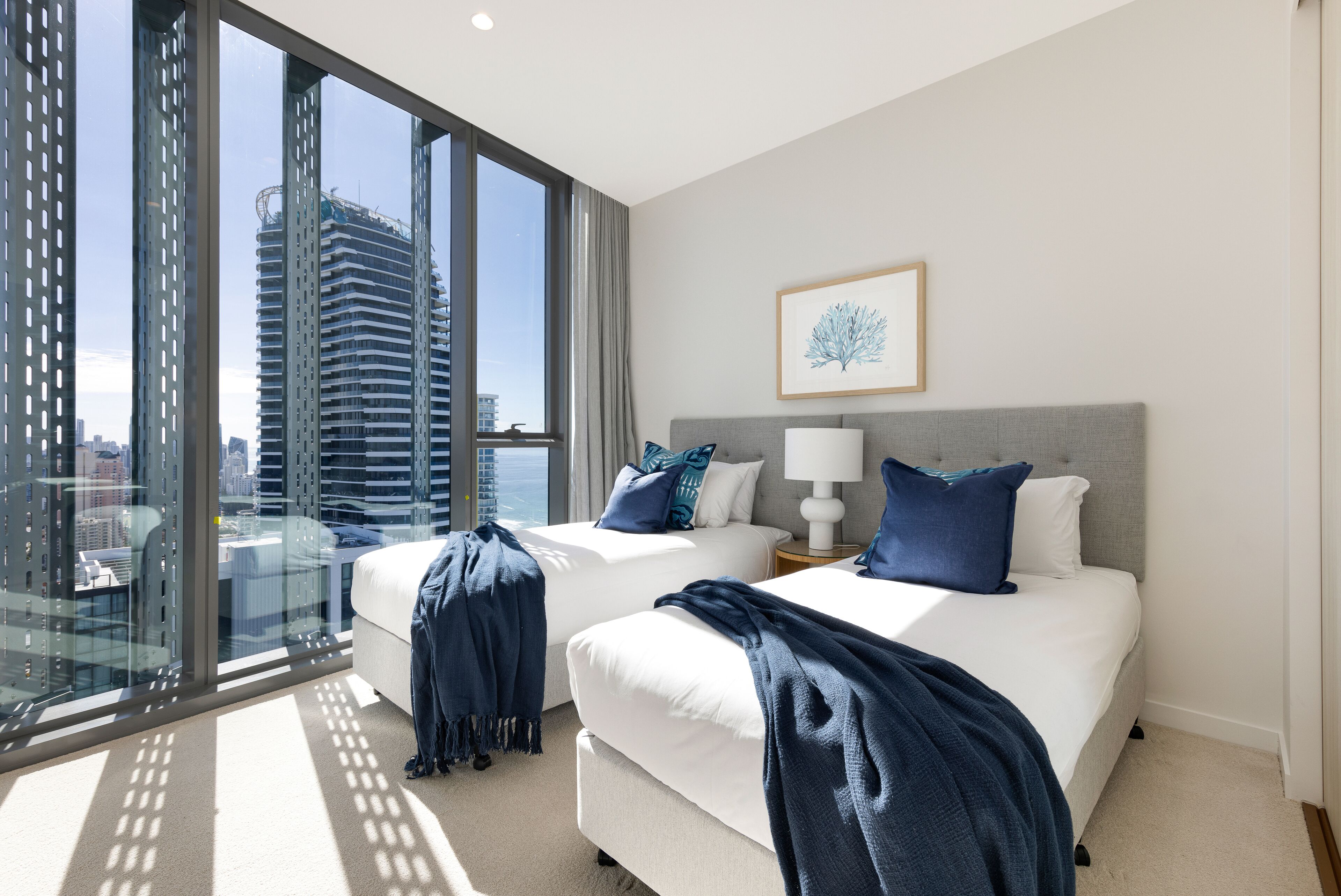 A modern hotel room with two beds, a city view, and a framed artwork on the wall.