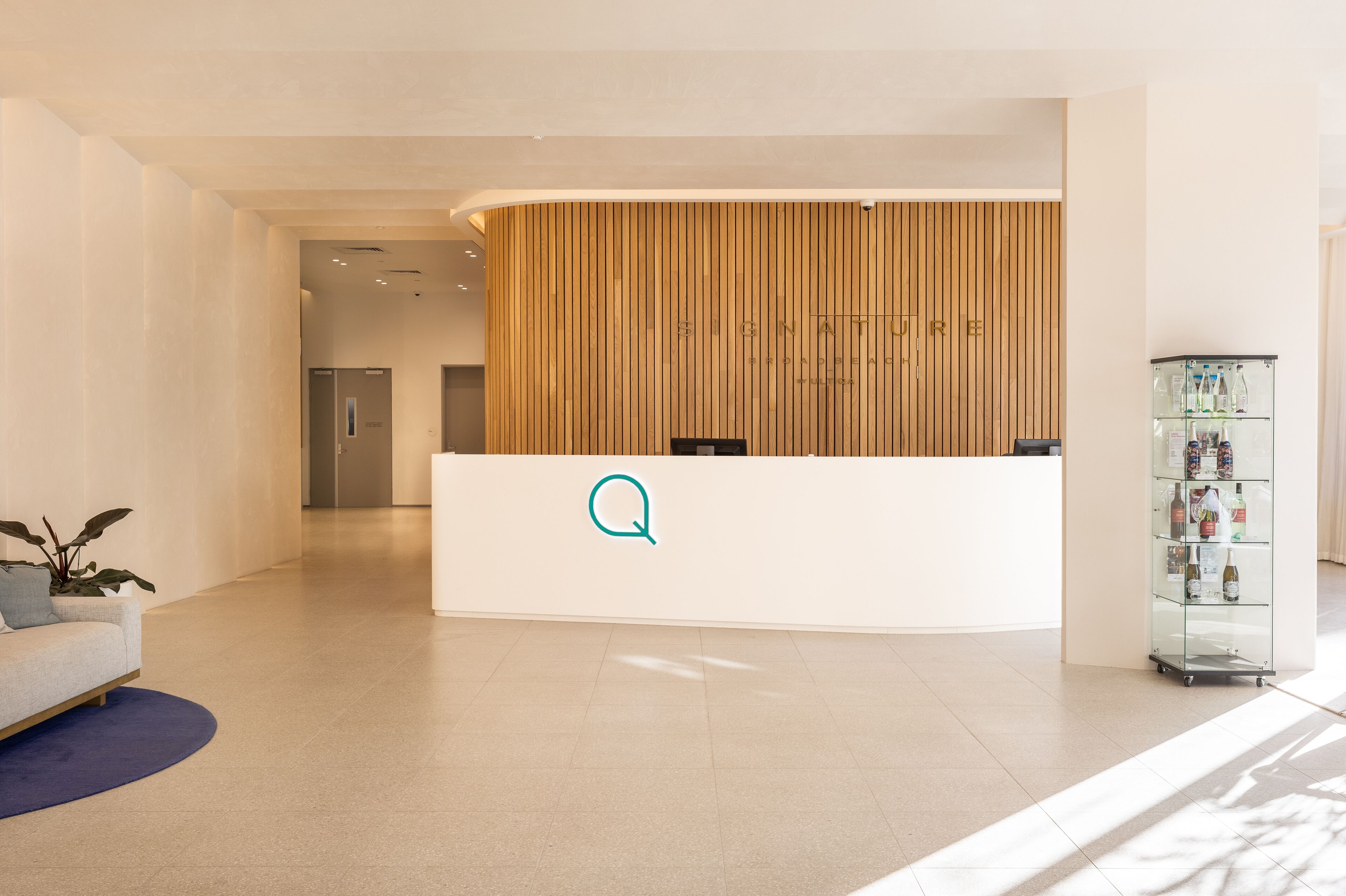 A reception area with a wooden panel wall, a reception desk with a logo, a glass display case with items, and a sofa with a plant.