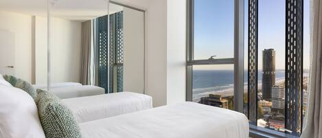 A modern hotel room with two beds, a large window with a city view, and a sliding glass door.