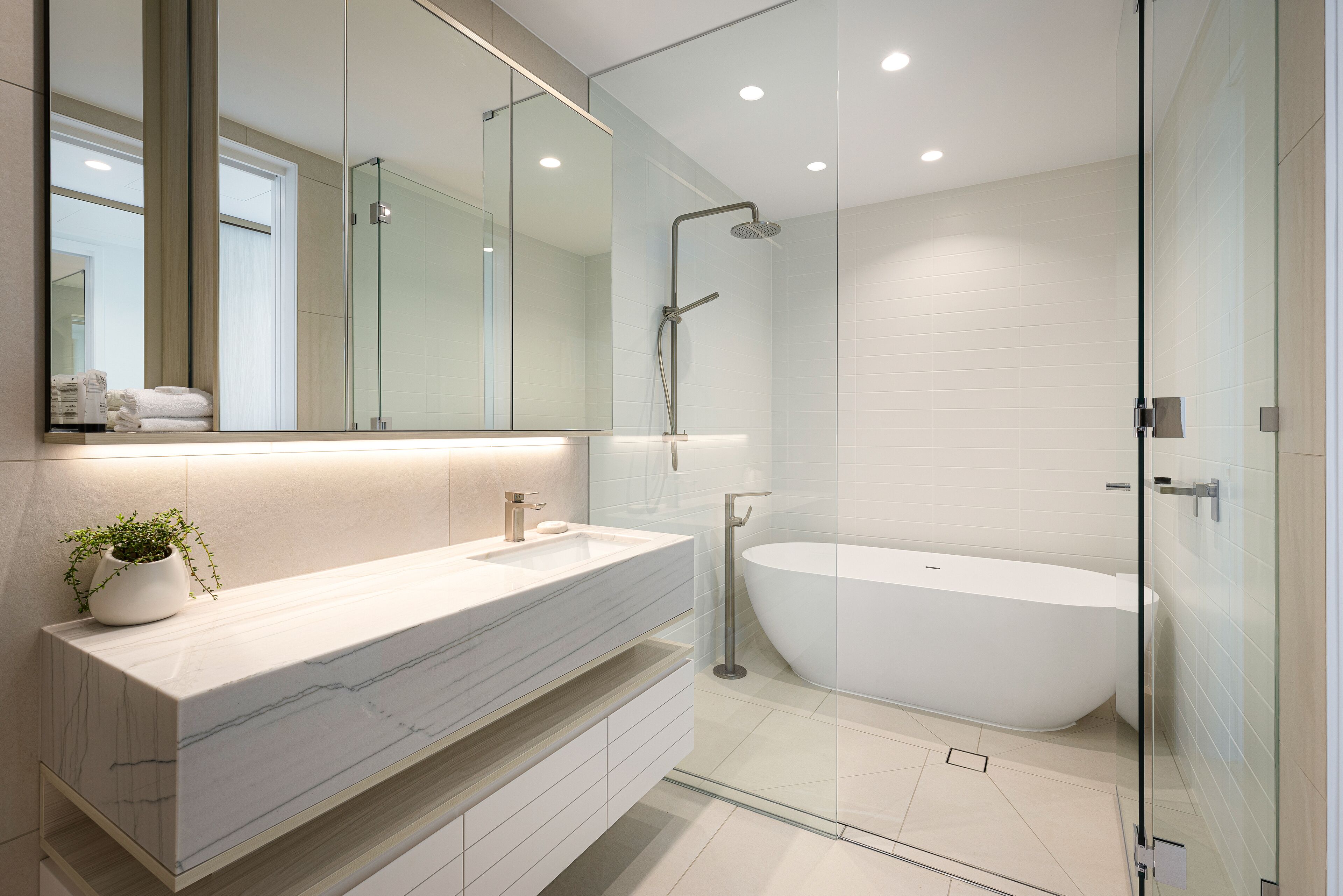 A modern bathroom with a large mirror, a white bathtub, and a glass shower enclosure.