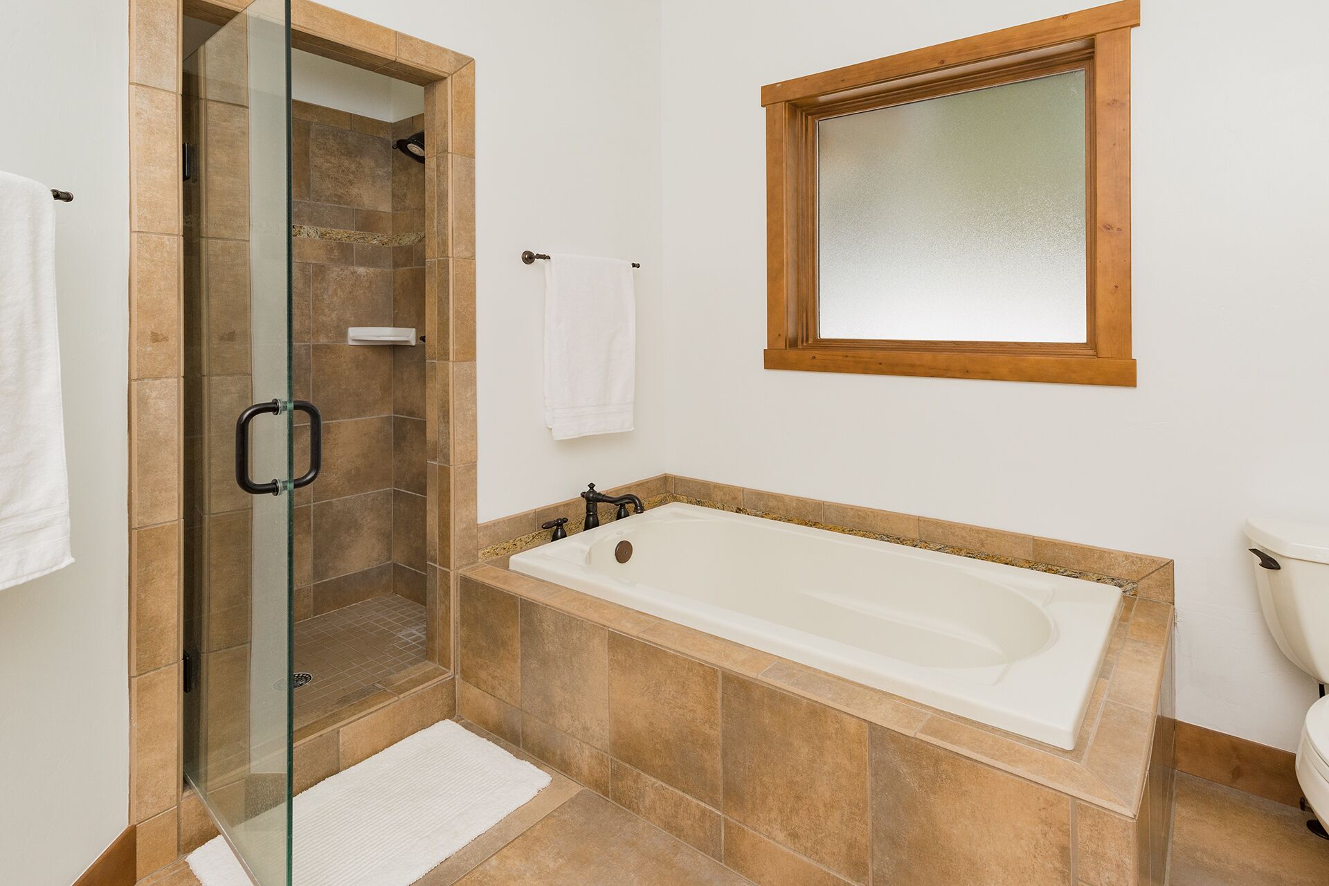 A bathroom with a glass-enclosed shower, a freestanding bathtub, and a window above the sink.