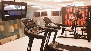 Ein Fitnessraum mit Laufbändern, einer Gewichtbank und einem Fernseher, der Fitnessvideos zeigt.