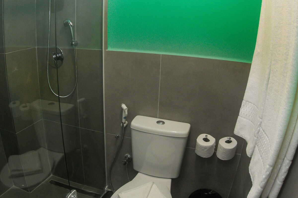 A bathroom with a glass-enclosed shower, a toilet, and two rolls of toilet paper.