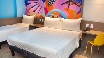 A hotel room with two single beds, a large bed, a desk with a chair, and a colorful abstract wall art.