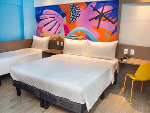 A hotel room with two single beds, a large bed, a desk with a chair, and a colorful abstract wall art. - Ibis Styles Garanhuns (Garanhuns)