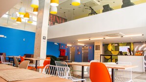 A modern restaurant with high ceilings, yellow and white pendant lights, and a mix of orange and white chairs. - Ibis Styles Garanhuns (Garanhuns)