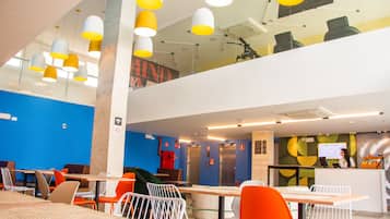 A modern restaurant with high ceilings, yellow and white pendant lights, and a mix of orange and white chairs.
