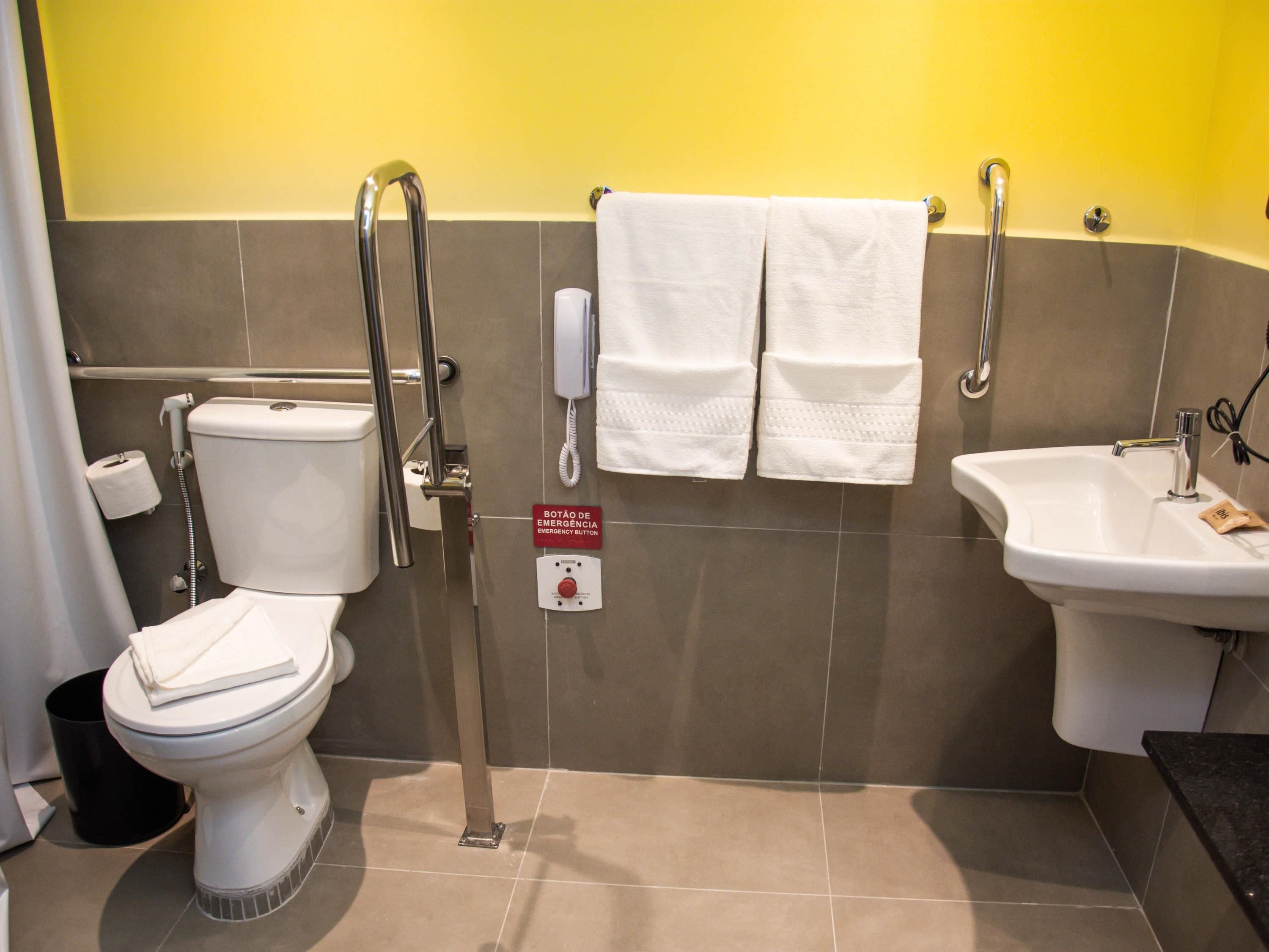 A bathroom with a toilet, bidet, and sink, equipped with a handrail and emergency button.