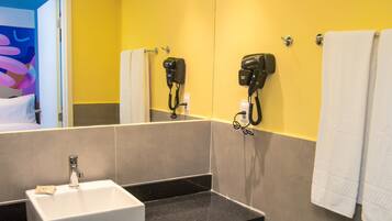 Un baño con un lavabo blanco, dos secadores de pelo fijados en la pared y un perchero con dos toallas.