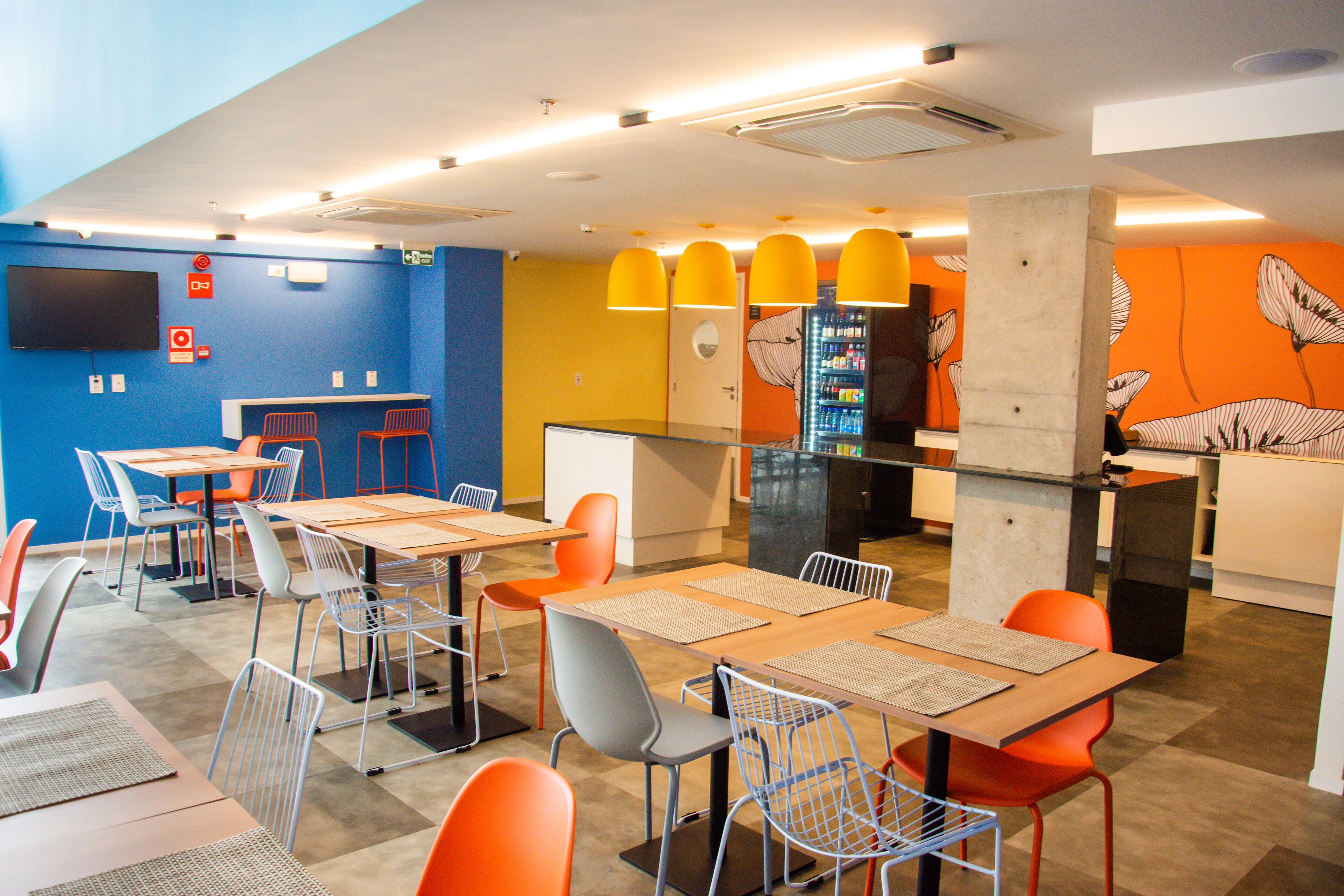 Um restaurante moderno com mesas, cadeiras, balcão e televisão na parede.