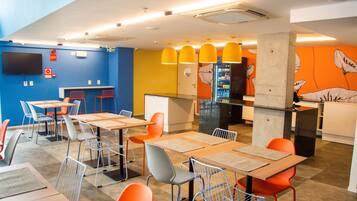 Um restaurante moderno com mesas, cadeiras, balcão e televisão na parede.