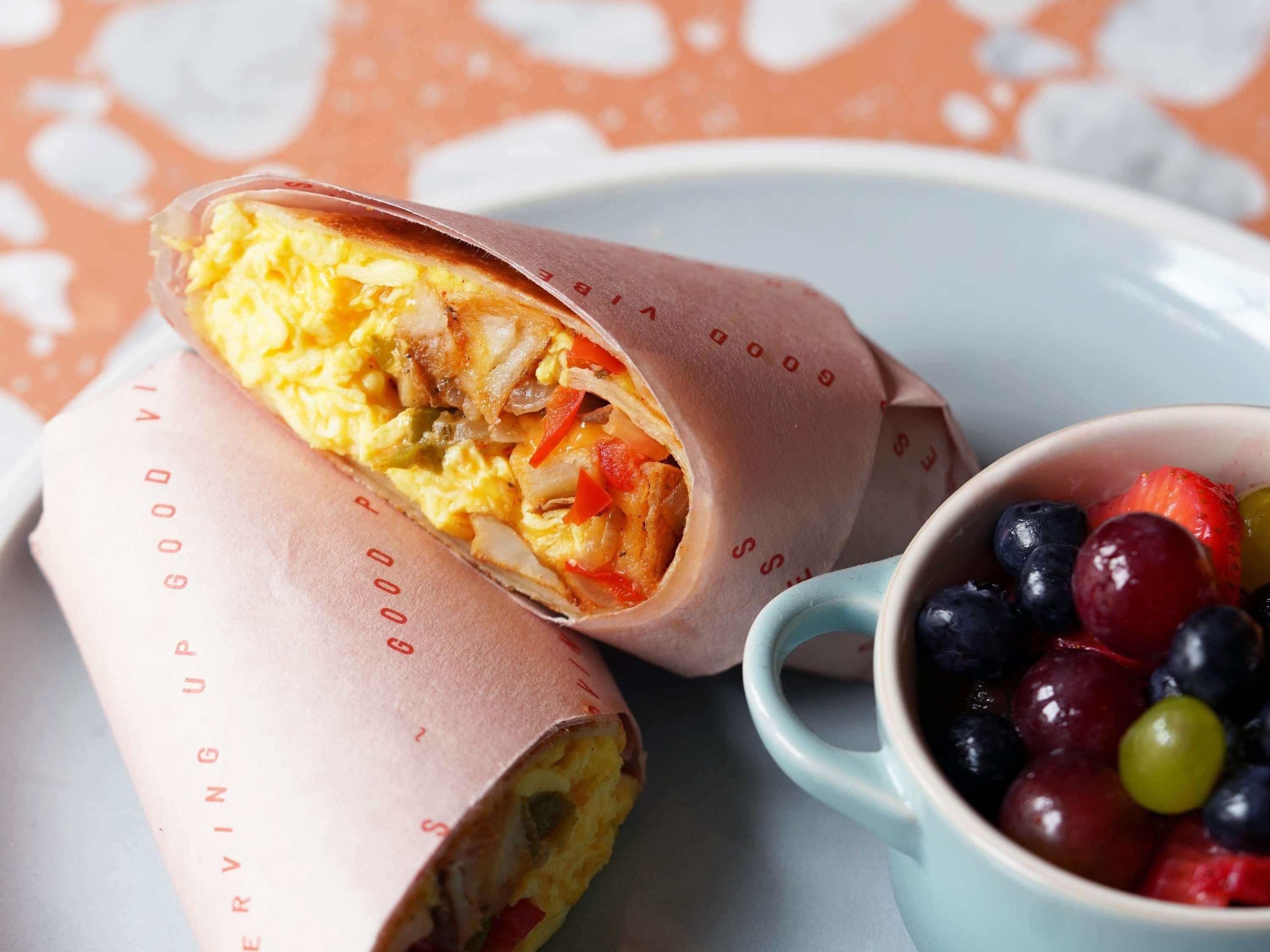 A wrapped food item, possibly a burrito, with a cup of mixed berries beside it.