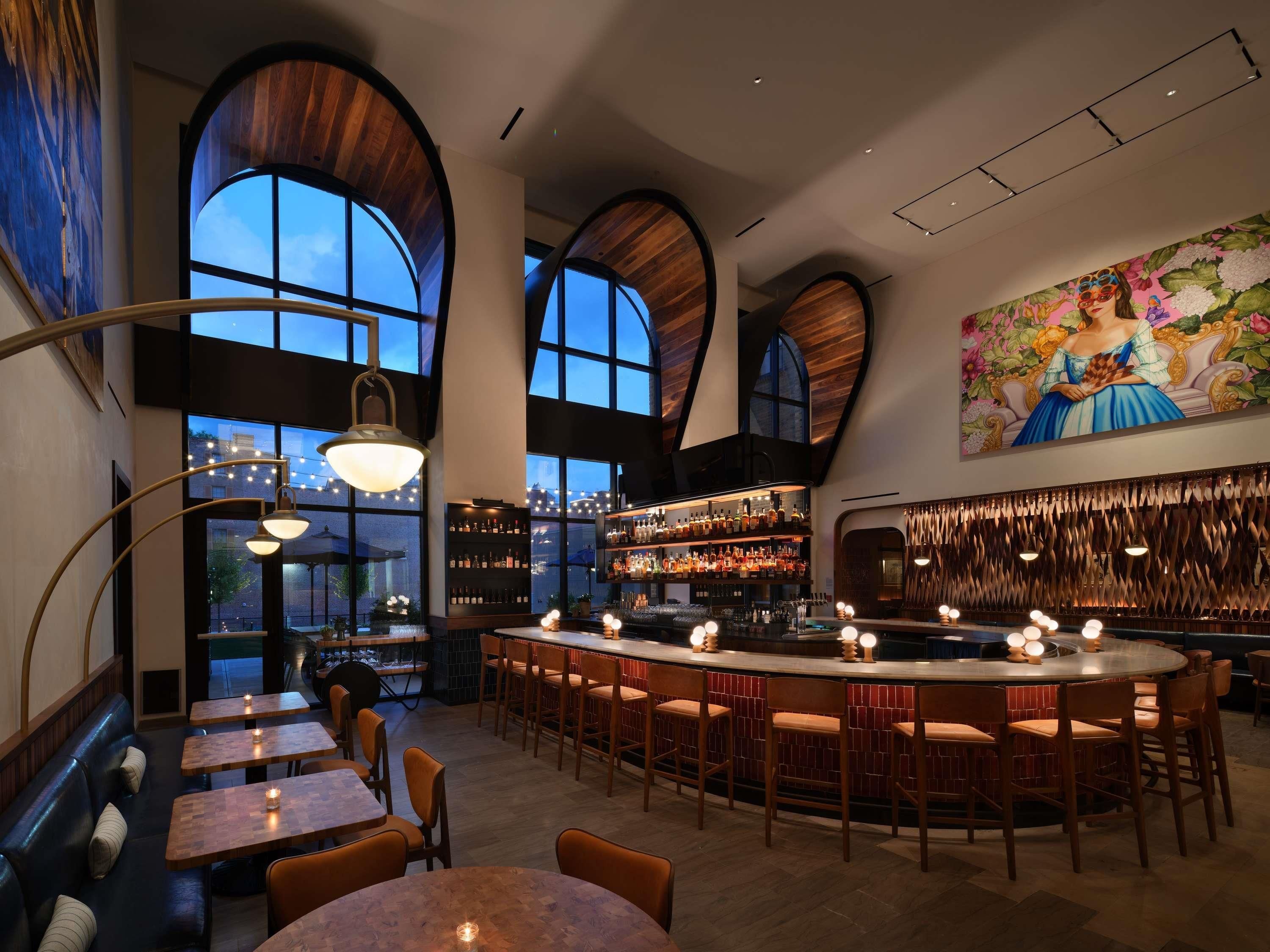Un espace bar doté de hauts plafonds en bois, d’une grande fresque murale et de différents types de sièges, notamment des tables et des tabourets de bar.