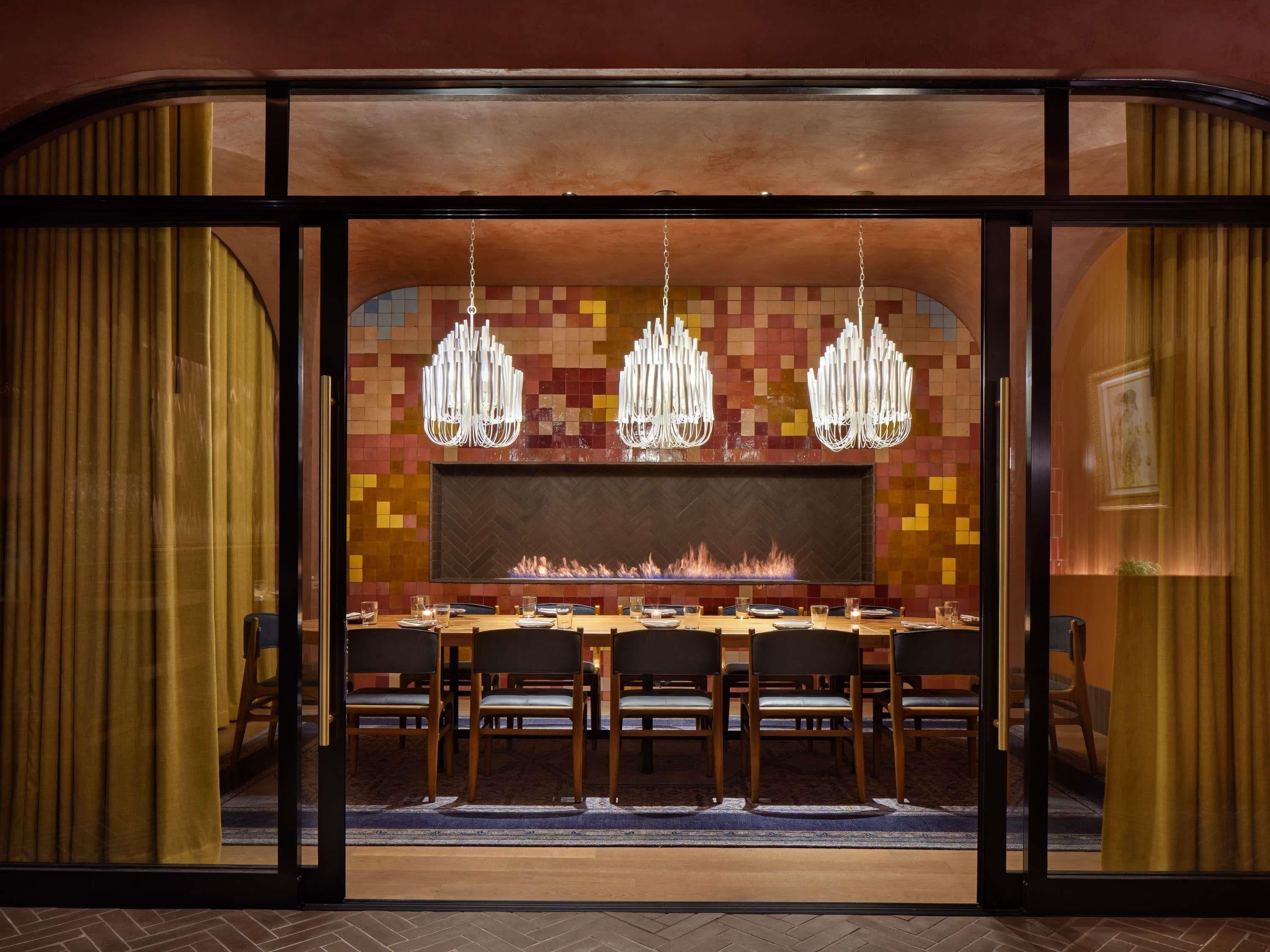 A dining area with a long table, chairs, a fireplace, and hanging light fixtures.