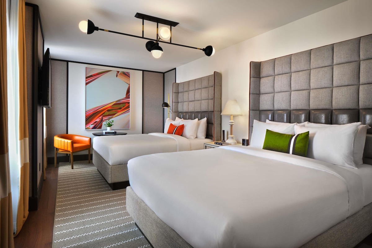 A hotel room with two beds, a sofa, a TV, and a large abstract painting.