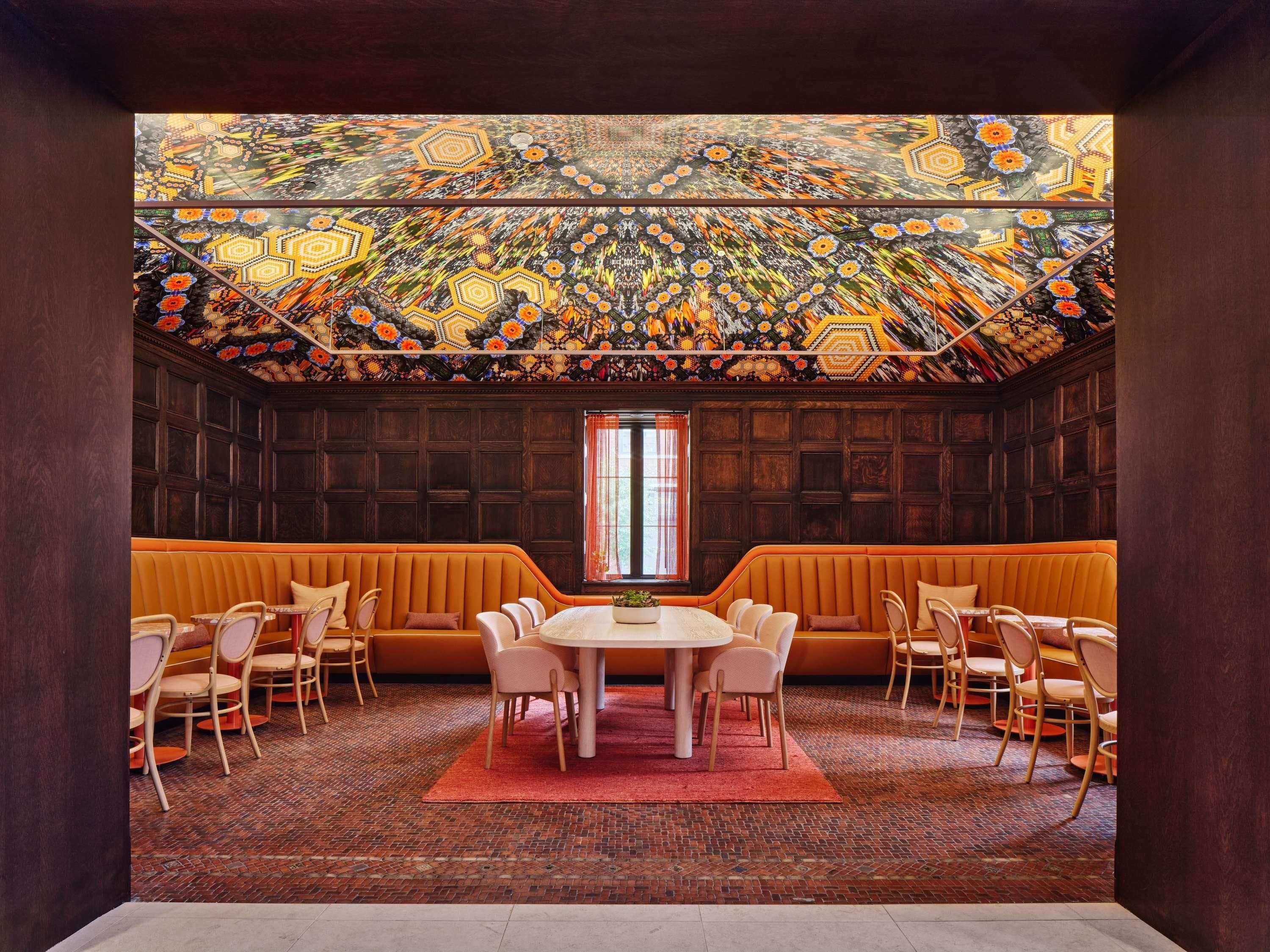 A dining area with a round table, orange upholstered bench, and wooden chairs.