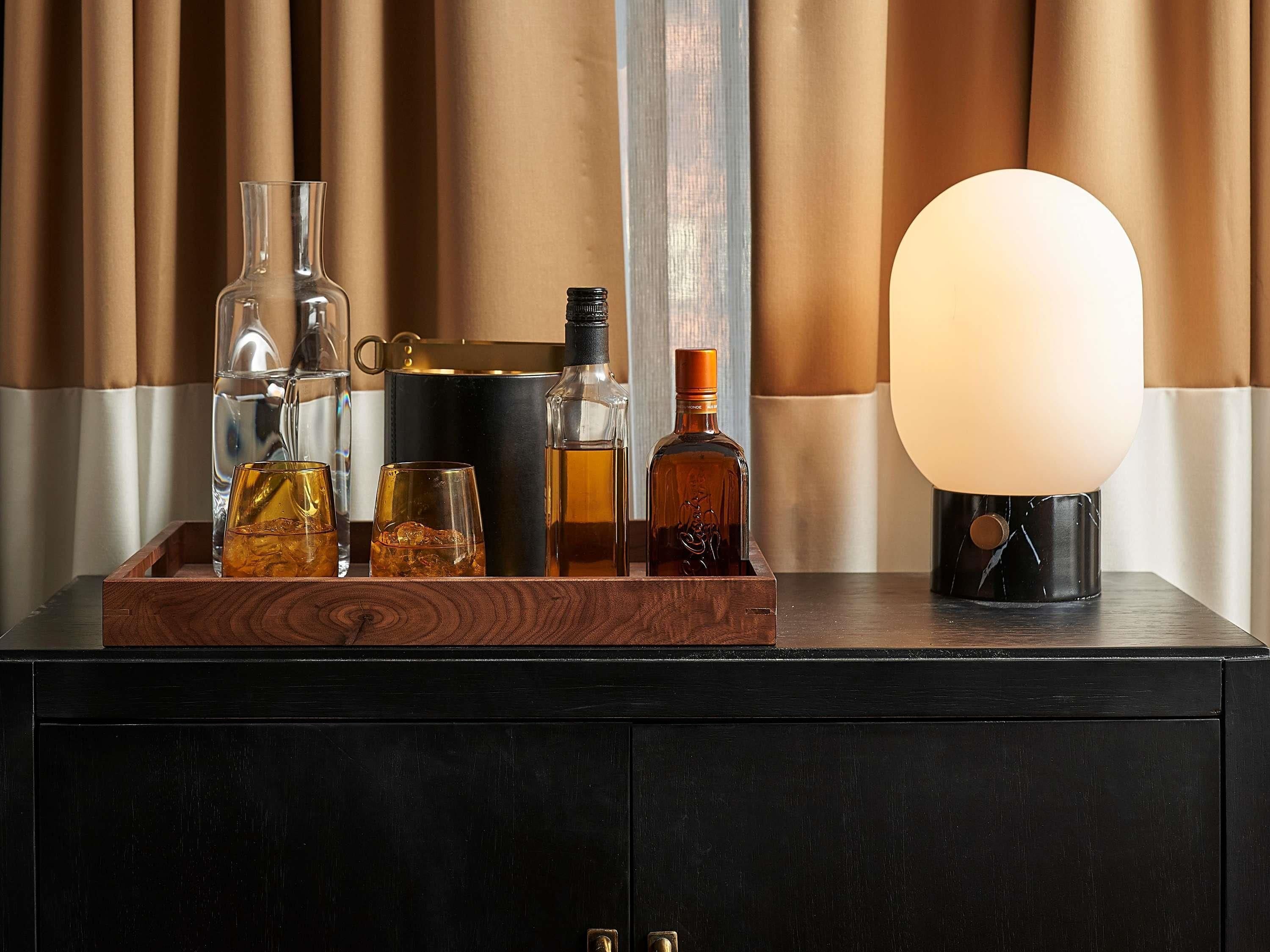 A wooden tray with various bottles and glasses on a dark cabinet against a curtain backdrop.