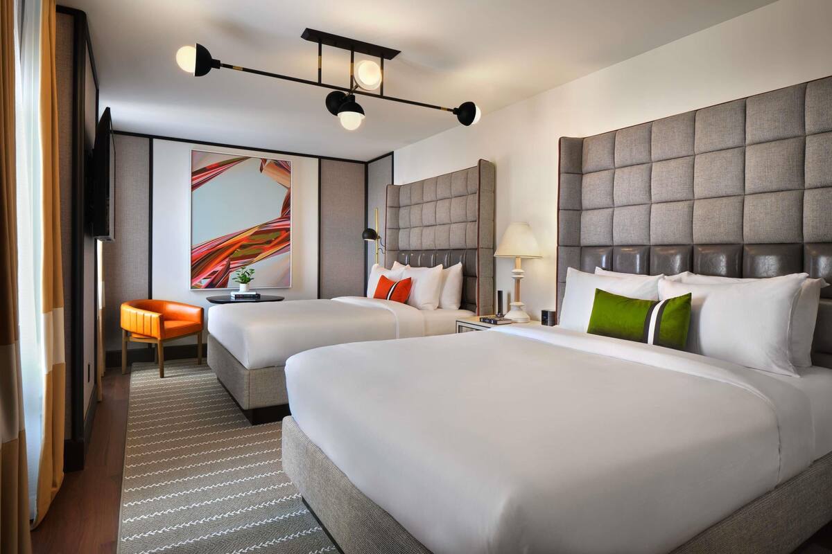 A hotel room with two beds, a sofa, a TV, and a large abstract painting.