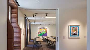 Een kunstgalerie met een modern interieur, bestaande uit een centrale tafel met stoelen, een kleurrijke muurschildering en ingelijste kunstwerken aan de muren.