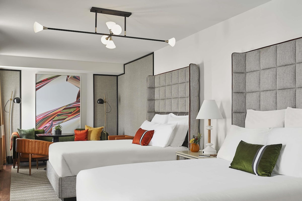 A hotel room with two beds, a large window, a modern ceiling light, and a view of a staircase.