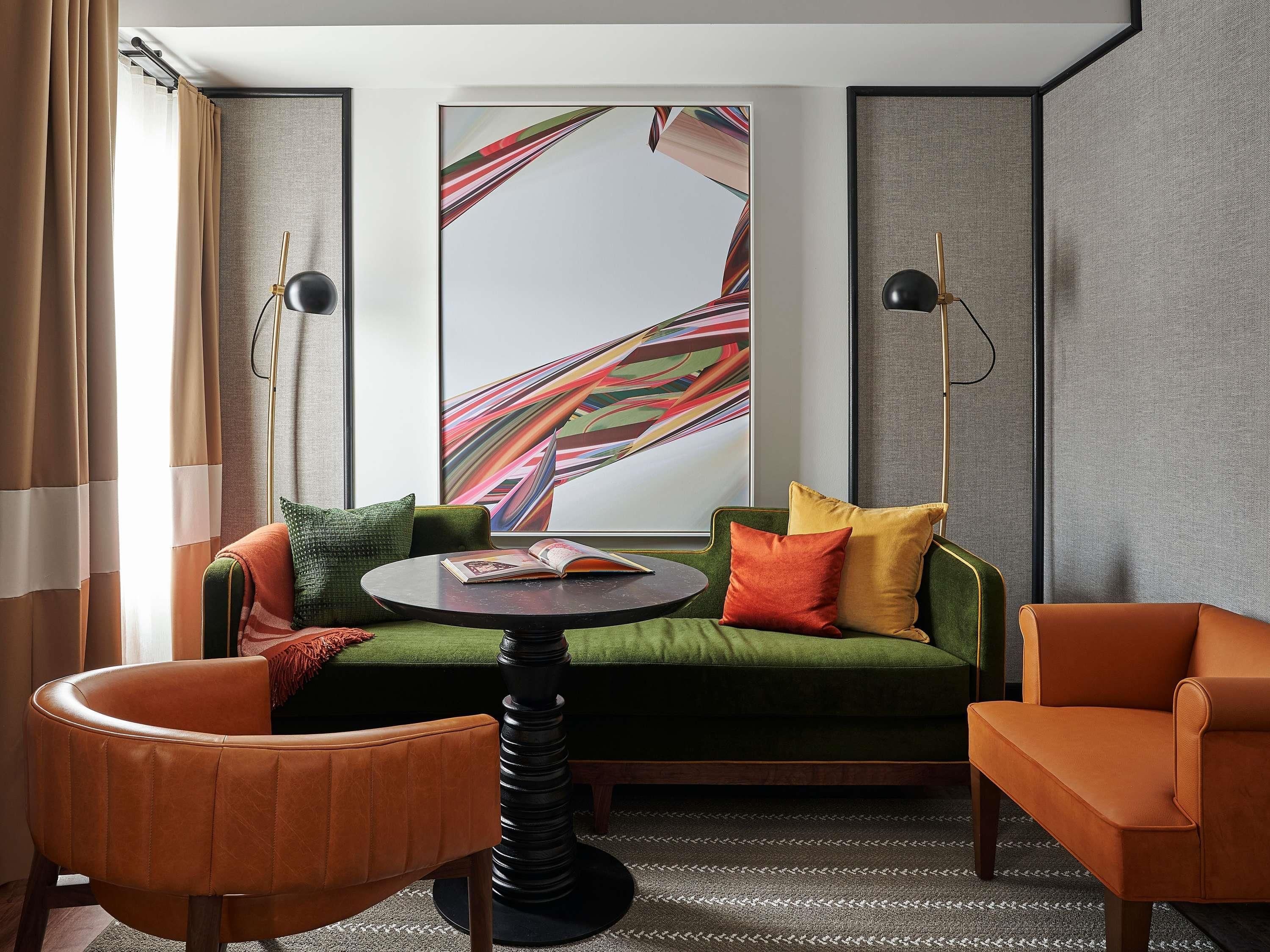 A modern room with a green sofa, two armchairs, a round table, and a large abstract painting on the wall.