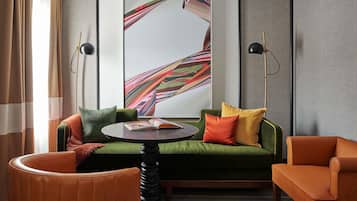 A modern room with a green sofa, two armchairs, a round table, and a large abstract painting on the wall.