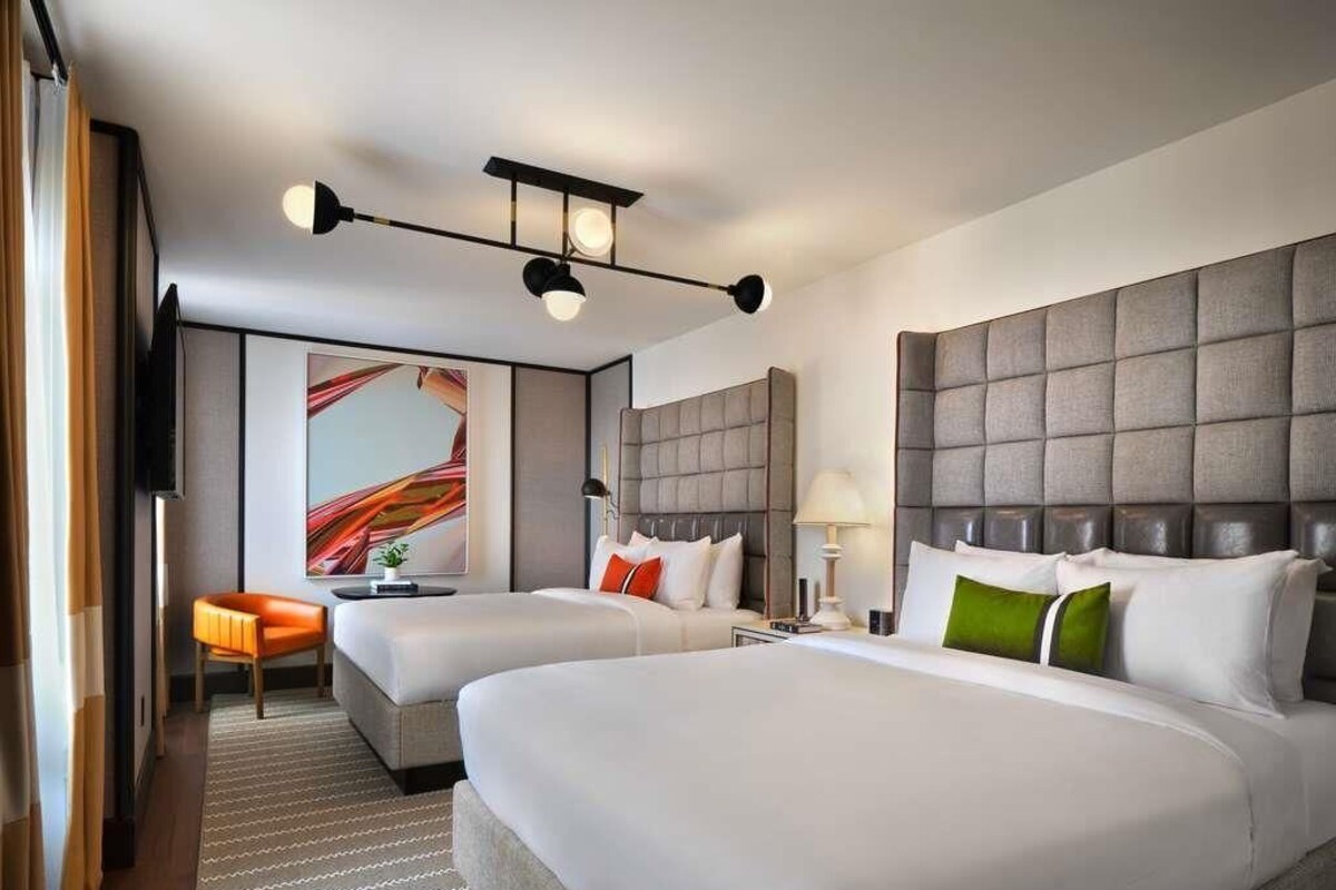 A hotel room with two beds, a sofa, a television, and a painting on the wall.