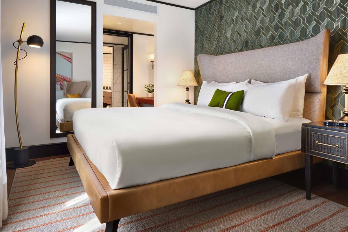 A hotel room with a large bed, a desk, a chair, a nightstand, and a mirror.