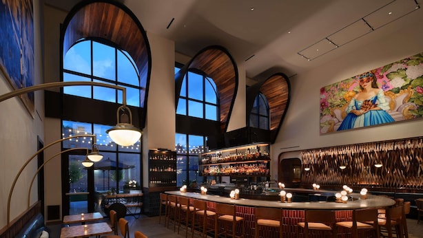 A bar area with high wooden ceilings, a large mural, and a variety of seating options including tables and bar stools.