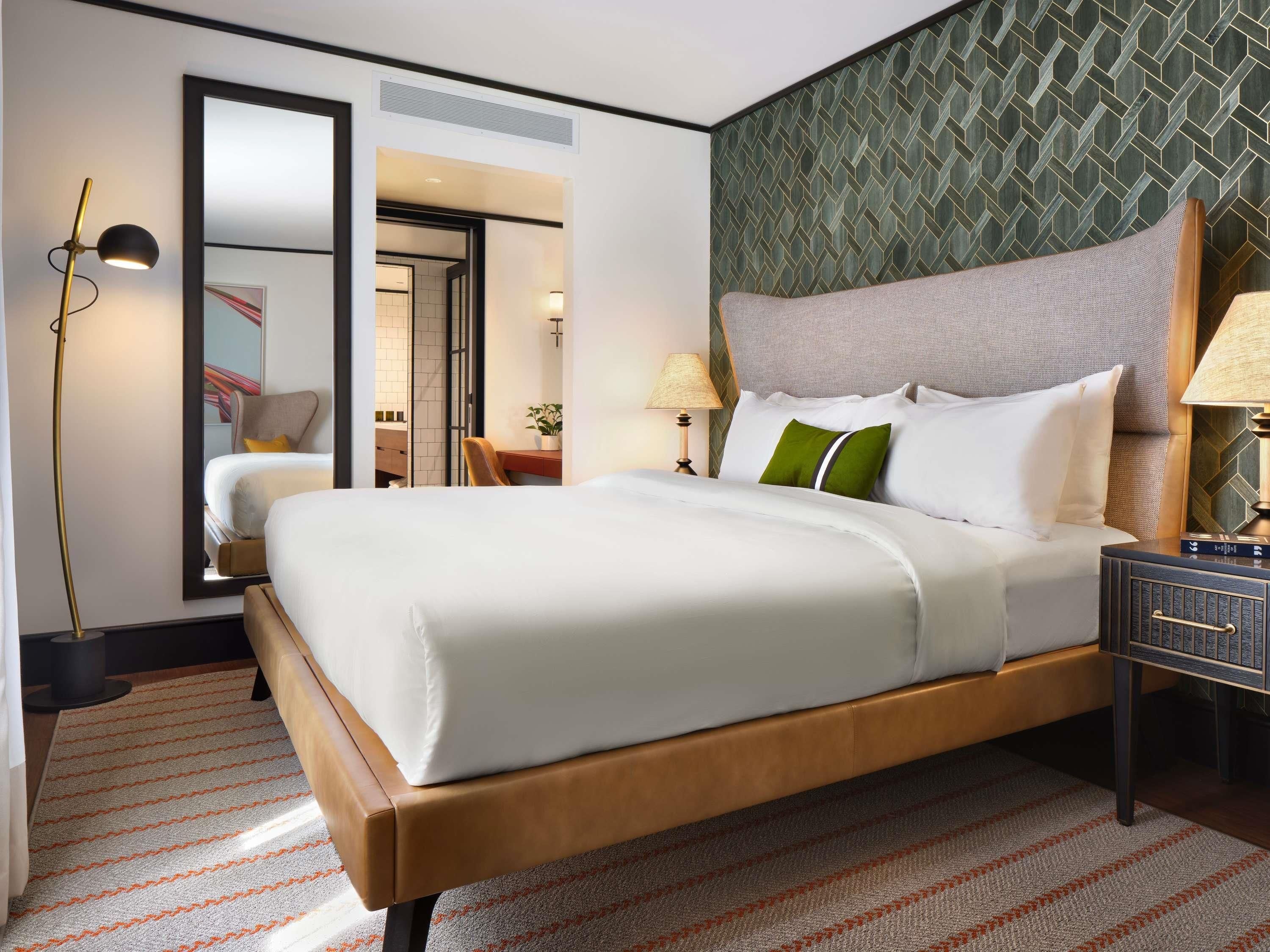 A hotel room with a large bed, a desk, a chair, a nightstand, and a mirror.