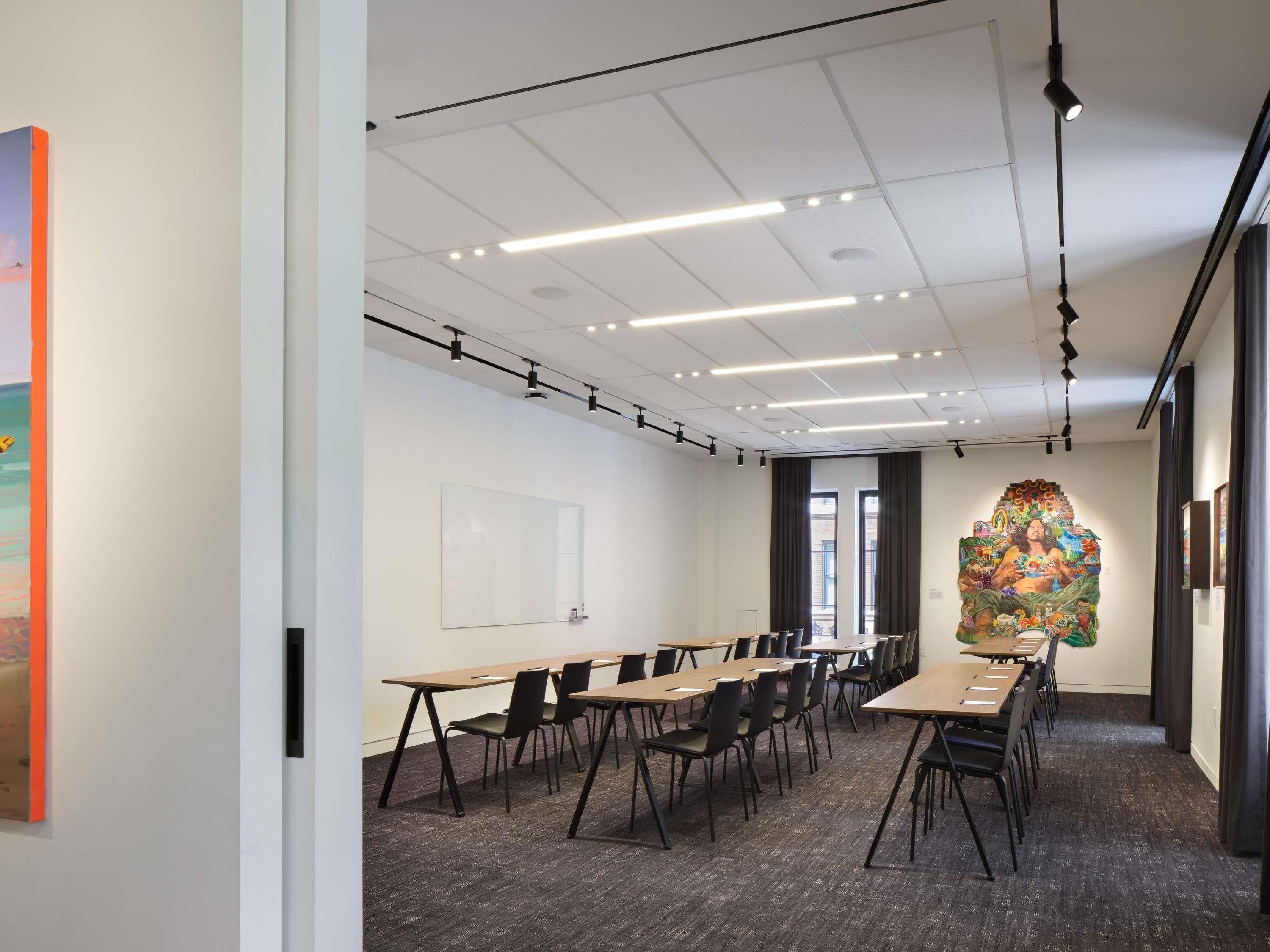 Une salle de conférence avec une longue table, des chaises, un tableau blanc et un grand tableau abstrait accroché au mur.