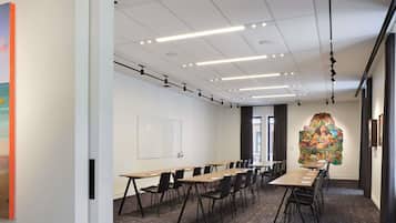 A conference room with a long table, chairs, a whiteboard, and a large abstract painting on the wall.