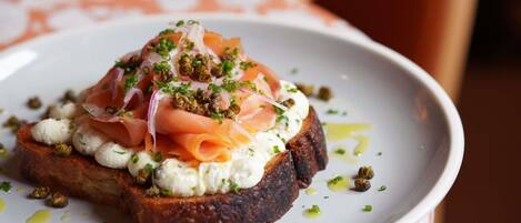Un plato con un sándwich cubierto de salmón ahumado, queso crema y alcaparras, decorado con cebollino.