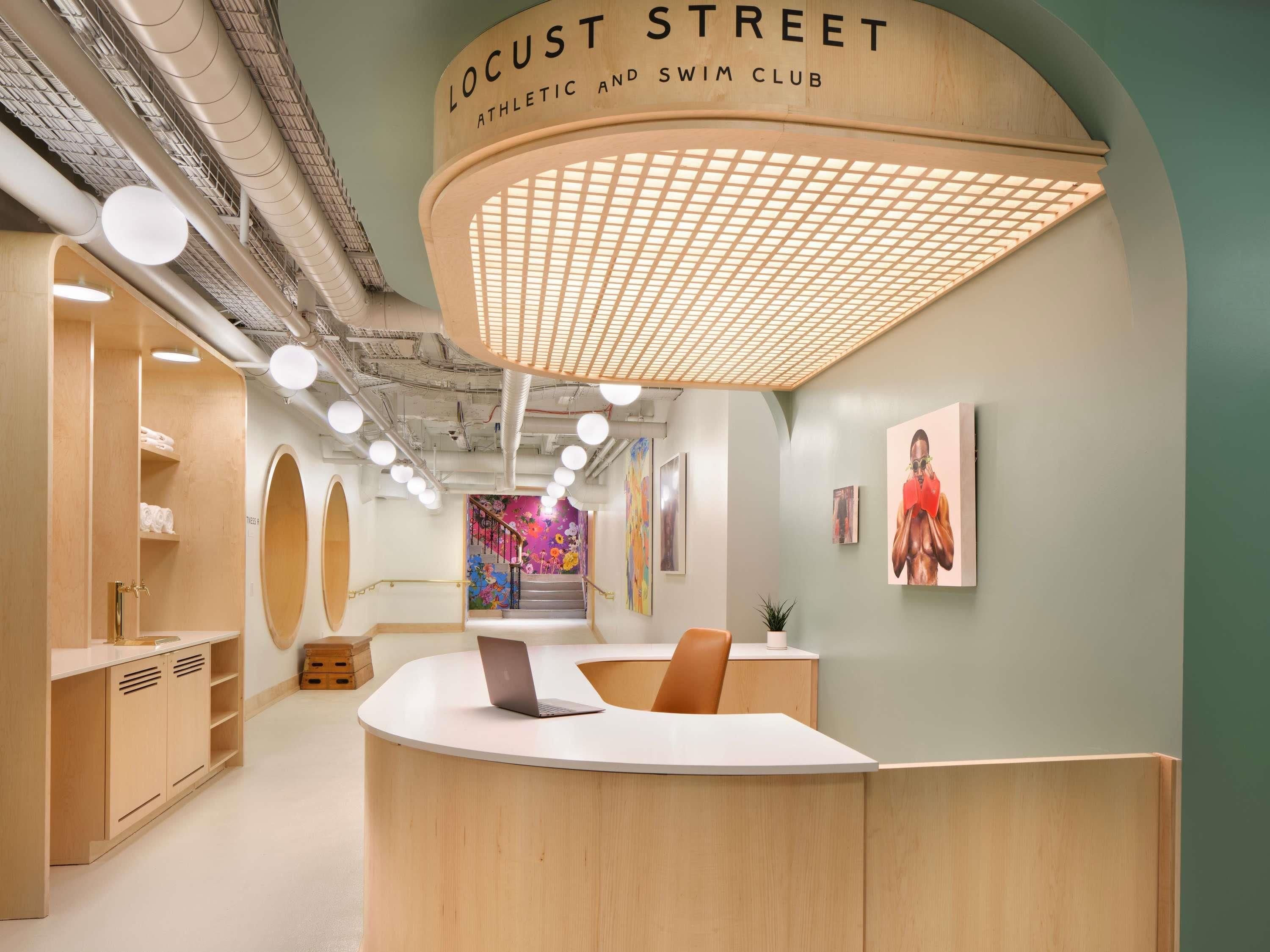 A reception area with a wooden counter, a staircase with a colorful mural, and a sign reading 'Locust Street Athletic and Swim Club.'