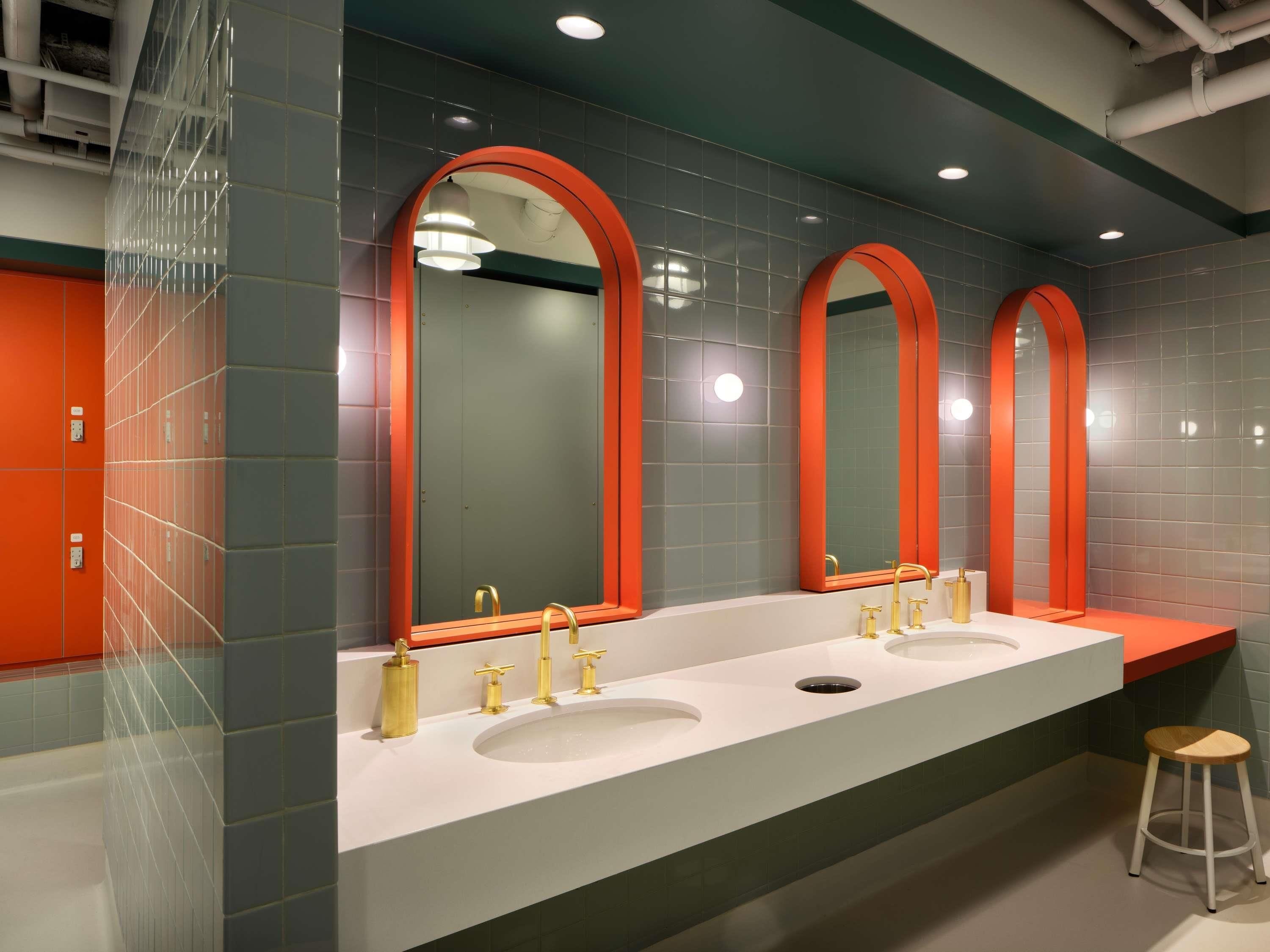 Un baño moderno con tres lavamanos, cada uno con un grifo dorado, y un espejo grande con marco naranja.