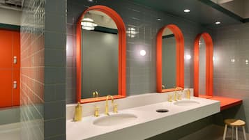 A modern bathroom with three sinks, each with a gold faucet, and a large mirror with an orange frame.