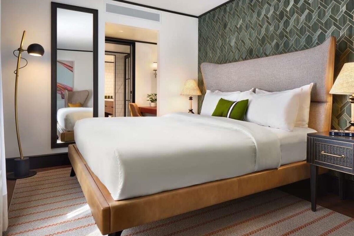 A hotel room with a bed, bedside tables, a lamp, a mirror, and a patterned wall.