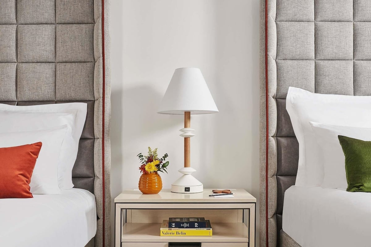 Une chambre d’hôtel avec deux lits, une table de chevet avec une lampe, un vase avec des fleurs et un livre.